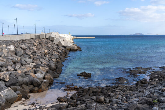 A picturesque coastal scene in Lanzarote, featuring a rocky embankment and crystal-clear ocean waters under a blue sky. - Powered by Adobe
