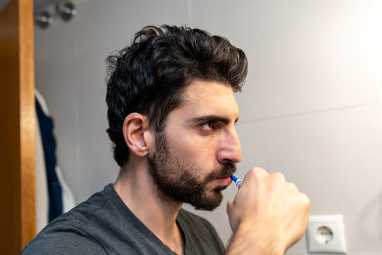 Young man brushing teeth in bathroom mirror, morning routine for oral hygiene and self-care