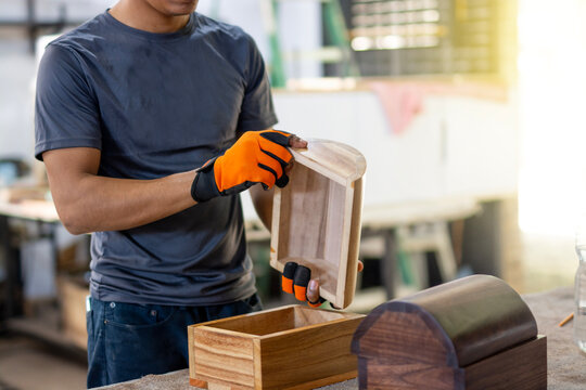 Cabinetmaker holding and inspecting a wooden box in the workshop. Carpenter with safety gloves working wood in the carpentry workshop