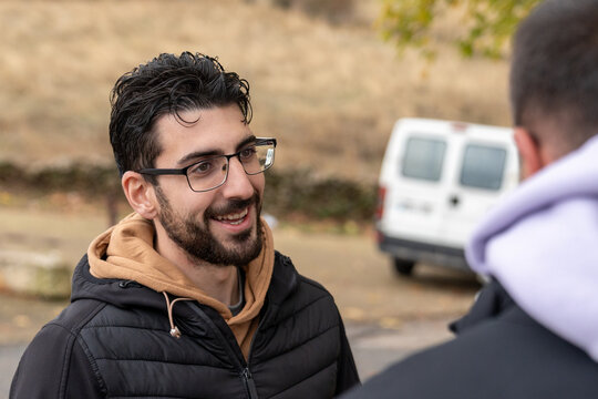 Young smiling man in glasses having conversation outdoors, expressing happiness and friendship during casual interaction