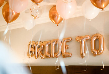 Festive bridal shower decor with rose-gold letter balloons spelling bride to, surrounded by...