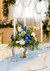 Elegant wedding table setting with blue and white floral centerpiece, candles, and refined decor. Romantic celebration atmosphere with fresh flowers, soft lighting, and sophisticated details