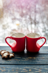 two heart shaped mugs with tea on the background of a window in winter

