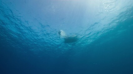 Low angle underwater shot looking up at a small boat with a SCUBA Diver splashing into the water
