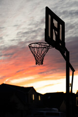 A warm multi colored reds and purples sunset behind a basketball hoop © Cavan