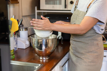 Woman sifting the flour into a metal bowl for making dough.