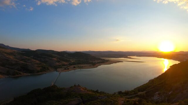 A sunset aerial flying backward over Studen Kladenets Reservoir in the Eastern Rhodopes, revealing the low sun over the water and the Lisytsite suspension bridge &mdash; the longest hanging bridge in BG