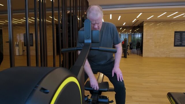 A Older Caucasian Man Walks Up To A Rowing Machine And Begins Exercising In A Indoor Gym.in slow motion