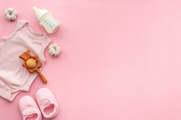 Baby bodysuit with wooden teethers and bottle of milk on pastel pink background, top view