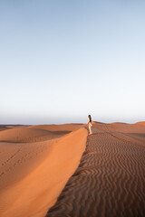 Woman traveling through desert dunes at sunset in oman