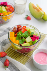 Close up fresh fruit salad in a bowl with mint leaf, red grape, avocado, melon, and dragonfruit on the table
