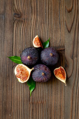 Purple ripe figs fruit and slices with green leaves top view on a wooden background