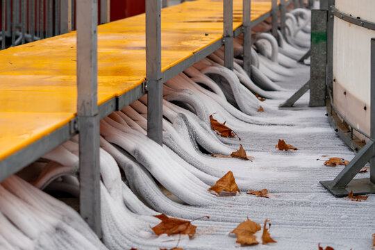 Frozen cooling hoses running beneath the ice rink structure, covered with frost and autumn leaves, showing the technical setup of the installation