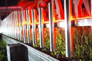 Fototapeta premium Modern stainless steel fence illuminated by red LED lights, creating a vibrant urban night atmosphere