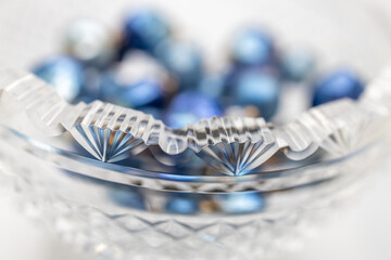 Defocused art style view of a beautiful scalloped edge antique lead crystal bowl containing chunky blue jewelry beads
