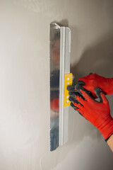 A masters hand in a red glove with a spatula does the work of leveling a wall with putty.