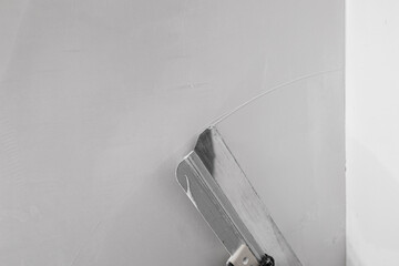 A masters hand in a red glove with a spatula does the work of leveling a wall with putty.