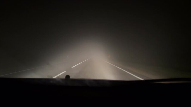 Night drive through heavy fog on an empty rural highway &mdash; low visibility road conditions captured from inside a car, concept of danger, isolation, and mystery