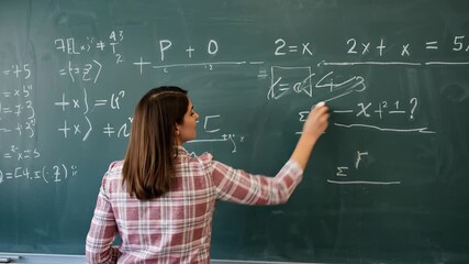 Dedicated female teacher or student writing complex mathematical equations and algebraic formulas on a traditional green blackboard with chalk, sym... - Powered by Adobe
