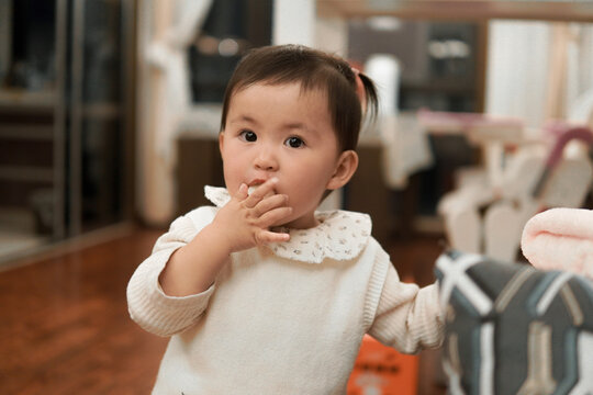 Cute Asian toddler girl eating a snack at home, wearing a white sweater with Peter Pan collar.