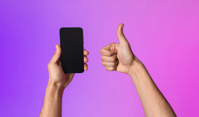 A millennial male displays a smartphone with an empty screen while giving a thumbs up, promoting a new mobile app. The scene is illuminated by neon lights, creating an inviting atmosphere.