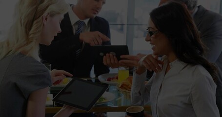 Meeting colleagues in business attire discussing plans at glass table, with tablets, coffee, fruit