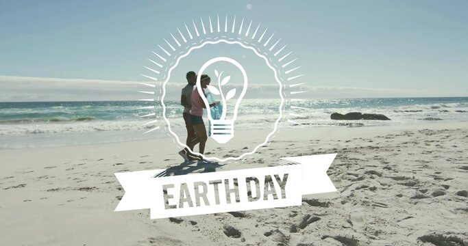 Walking couple wearing pink top and dark shorts along sandy shore, with white Earth Day graphic