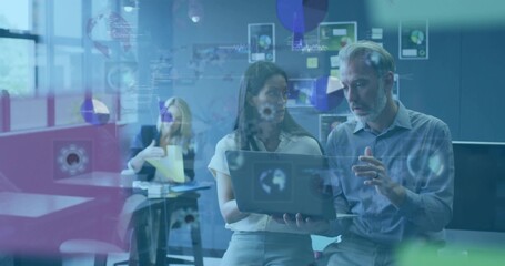 Collaborating two colleagues in business attire viewing laptop in office with glass showing data