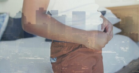 Standing boy wearing white top and rust shorts, clasping abdomen on bed, city skyline overlay