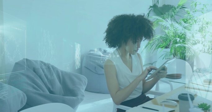 Holding tablet, woman in sleeveless white blouse focusing on screen at home desk with mug succulent
