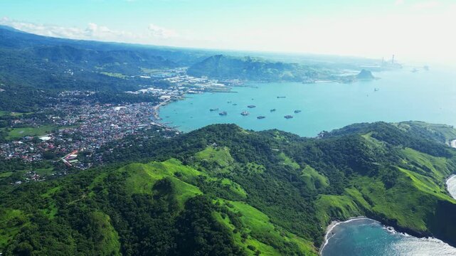 Pull‑out high aerial of Mariveles town in Bataan, seen from Nagbayog View Deck, revealing the coastal settlement, harbor, and surrounding lush green hills against the sea horizon.