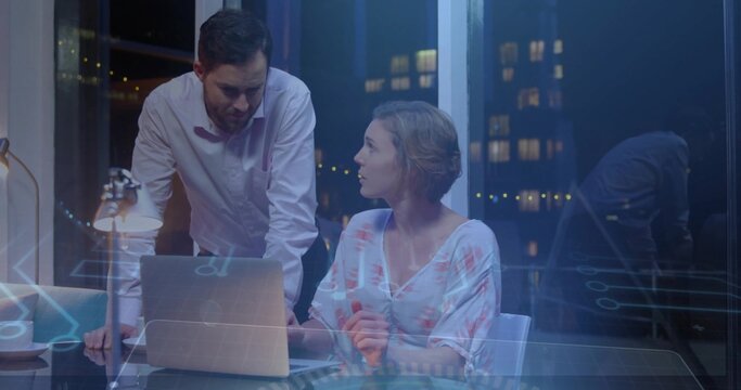 Discussing team in business attire leaning over glass table with laptop overlay in office at night