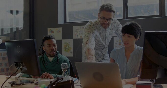 Pointing man in checkered shirt guiding team in light blouse, green hoodie at desk with laptop