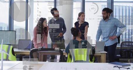 Reviewing team leaning around table in modern office, with laptops, safety vest, wind turbine