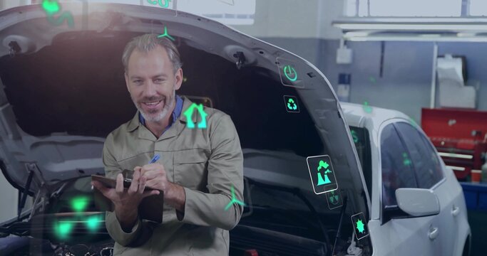 Leaning mechanic in coveralls holding tablet checking white car at workshop, showing green icons