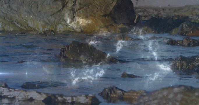 Naklejki Glistening dark boulder cluster catching low sun at coastal shore, with tide pools, nebula