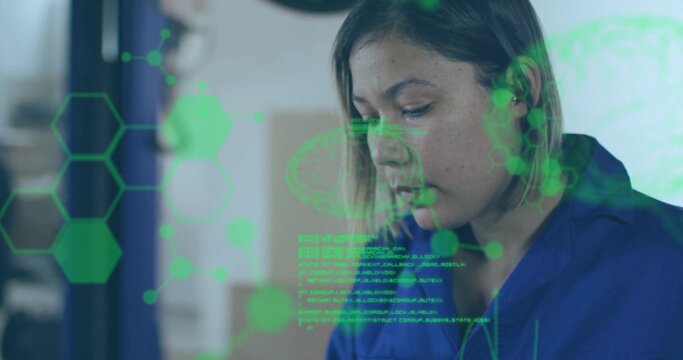 Concentrating female technician in blue coveralls examining screen at lab with green AR hexagons