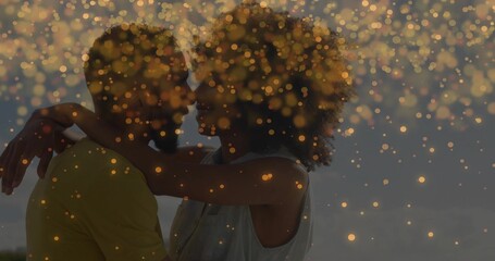 Naklejka premium Embracing couple holding close at beach at dusk, with yellow shirt sleeveless top and golden bokeh