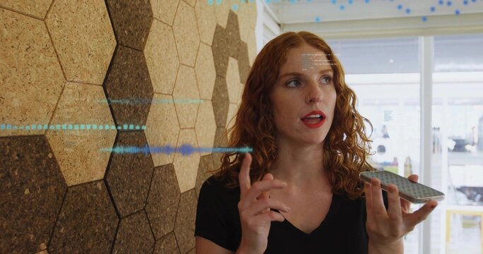Holding phone, redhead in black Vneck top talking by cork hexagons and window, waveform, copy space