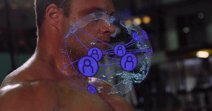 Turning shirtless man projecting holographic globe with user icons in dim gym interior