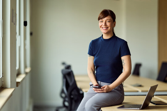 Smiling Business Woman Seated In Modern Office With Laptop And Phone
