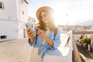 A beautiful woman in a hat stands in a busy square, holding a phone. A young tourist in sunglasses...