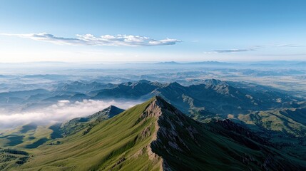 An aerial perspective showcases a dramatic, sharp ridge of a green mountain bathed in sunlight, with layers of misty, blue-hued mountains stretching into the di
