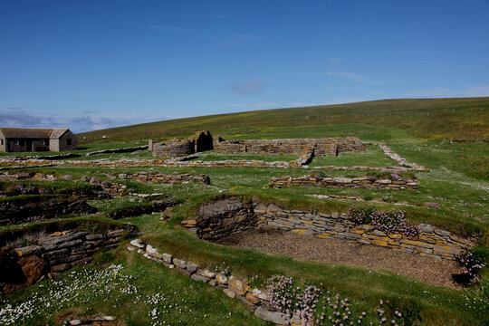 Ruins of the Brough of Birsay in Orkney, a ancient historic norse Viking settlement with weathered stone foundations set against rugged cliffs and bright blue coastal skies.