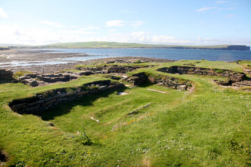 Ruins of the Brough of Birsay in Orkney, a ancient historic norse Viking settlement with weathered stone foundations set against rugged cliffs and bright blue coastal skies.