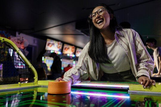 Laughing woman playing air hockey in arcade at night
