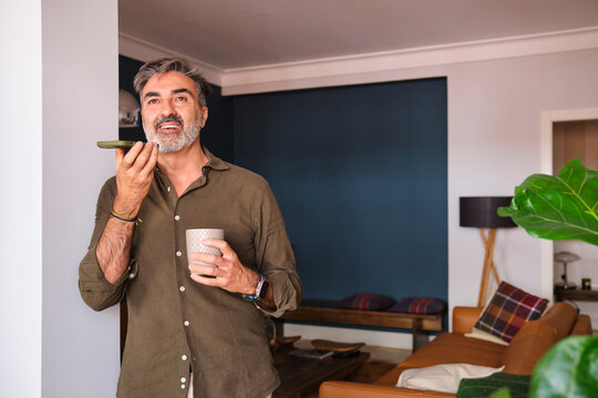 Man sending voice message on phone at home in living room