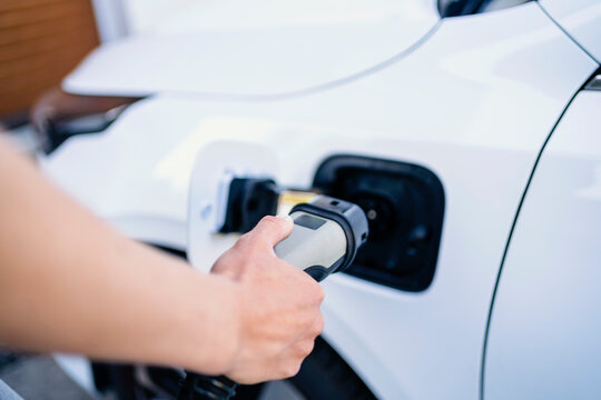 Hand of woman charging electric car with plug