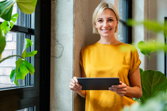 Smiling businesswoman with tablet in modern office near window