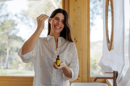 Woman applying facial serum with a pipette in a bright bathroom